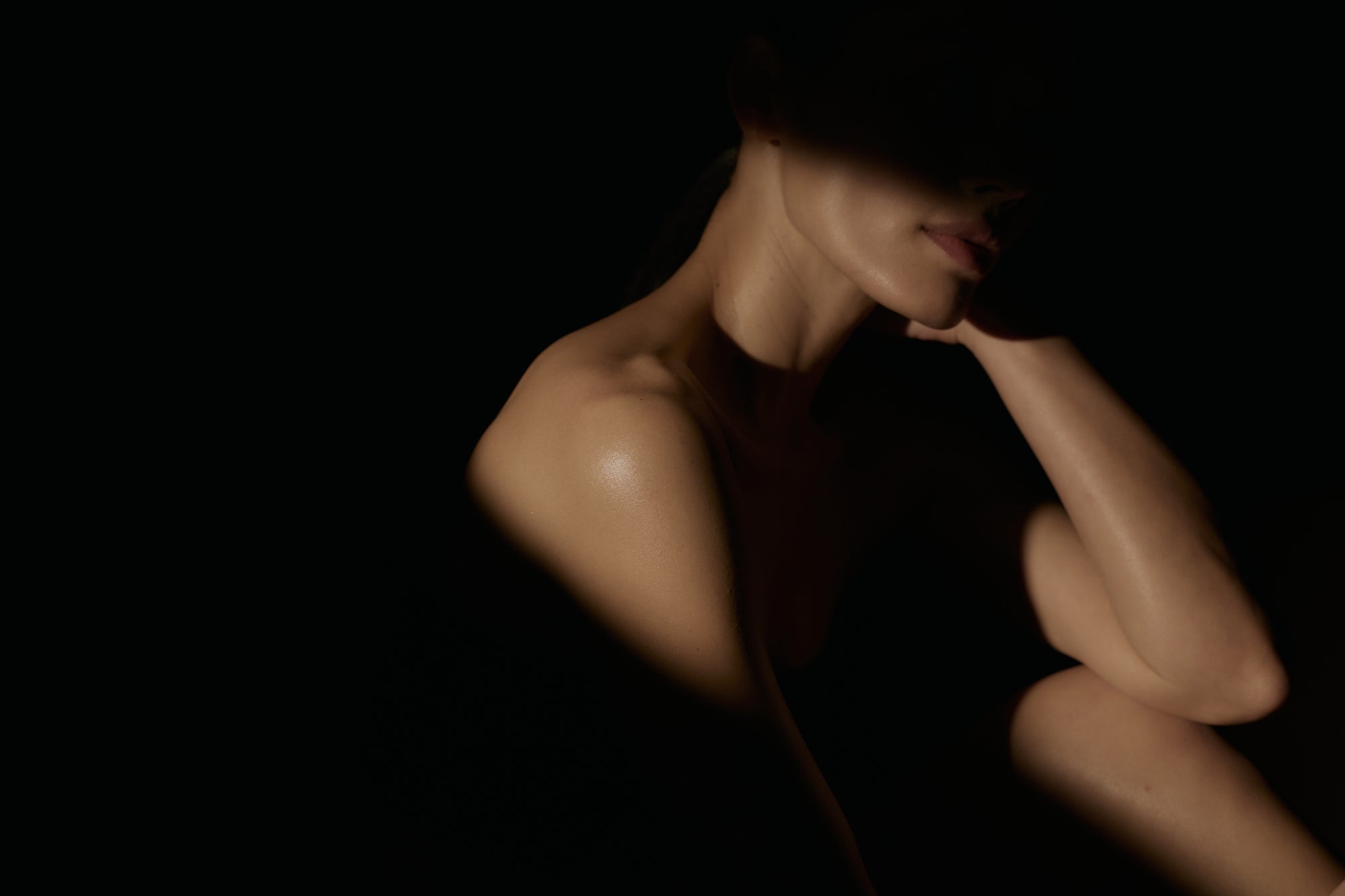 Naked person sitting in a dark room with minimal lighting