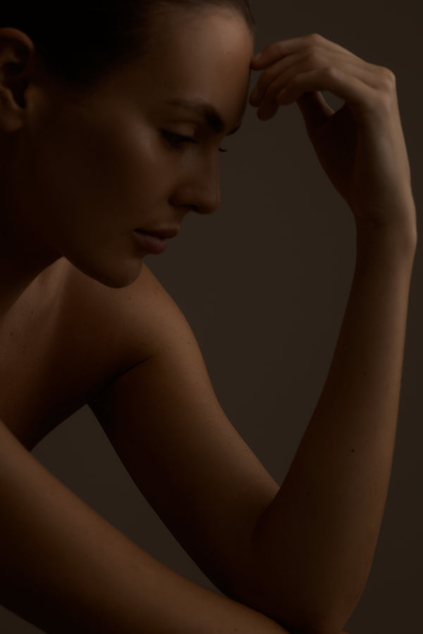 Naked woman with one arm raised against a dark background