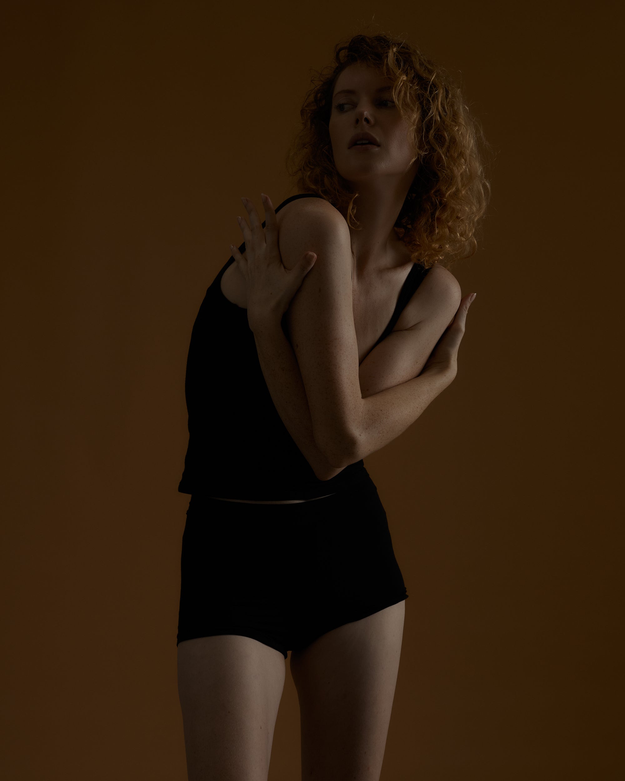 Woman in black shorts singlet against a brown background