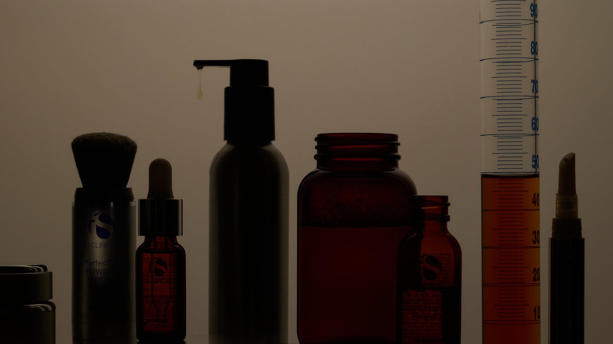 Silhouettes of various cosmetic bottles and containers against a dark background