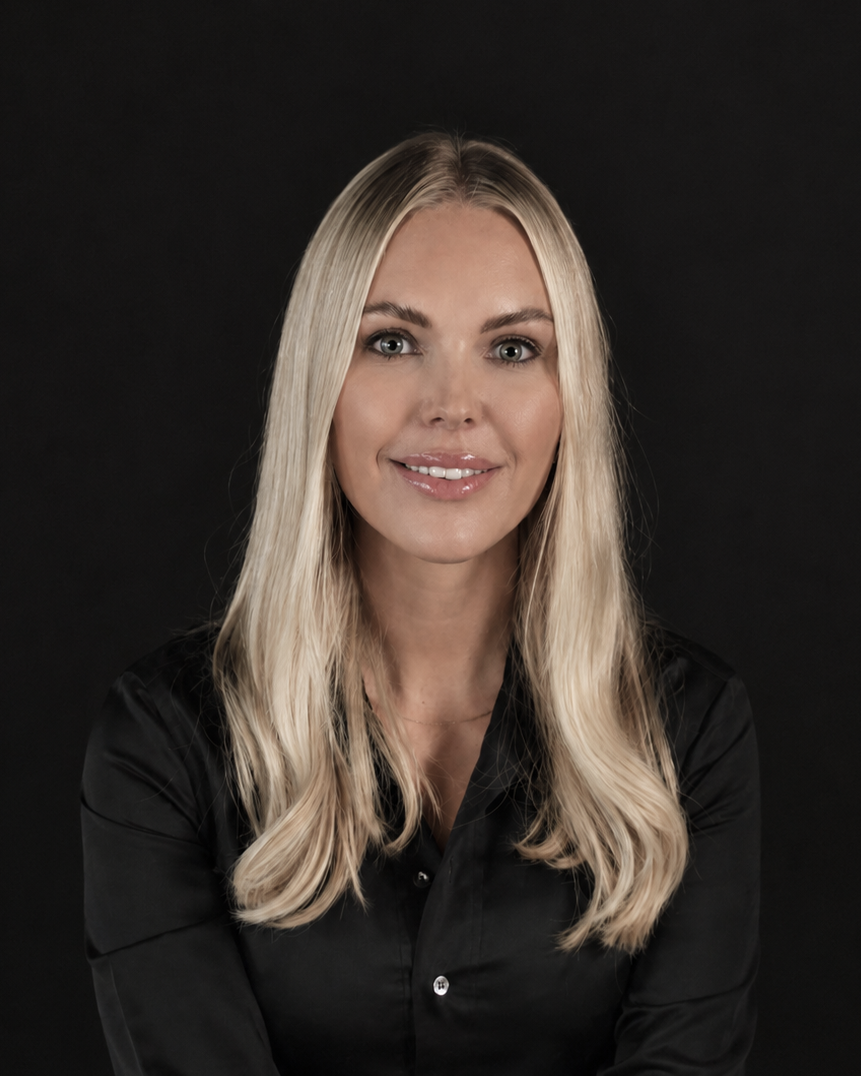 A blonde woman with long hair wearing a black satin button-up shirt, posing against a solid black background.