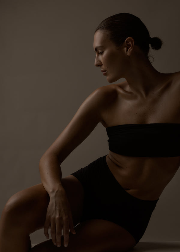 Woman in a black strapless top and black shorts sitting against a dark background