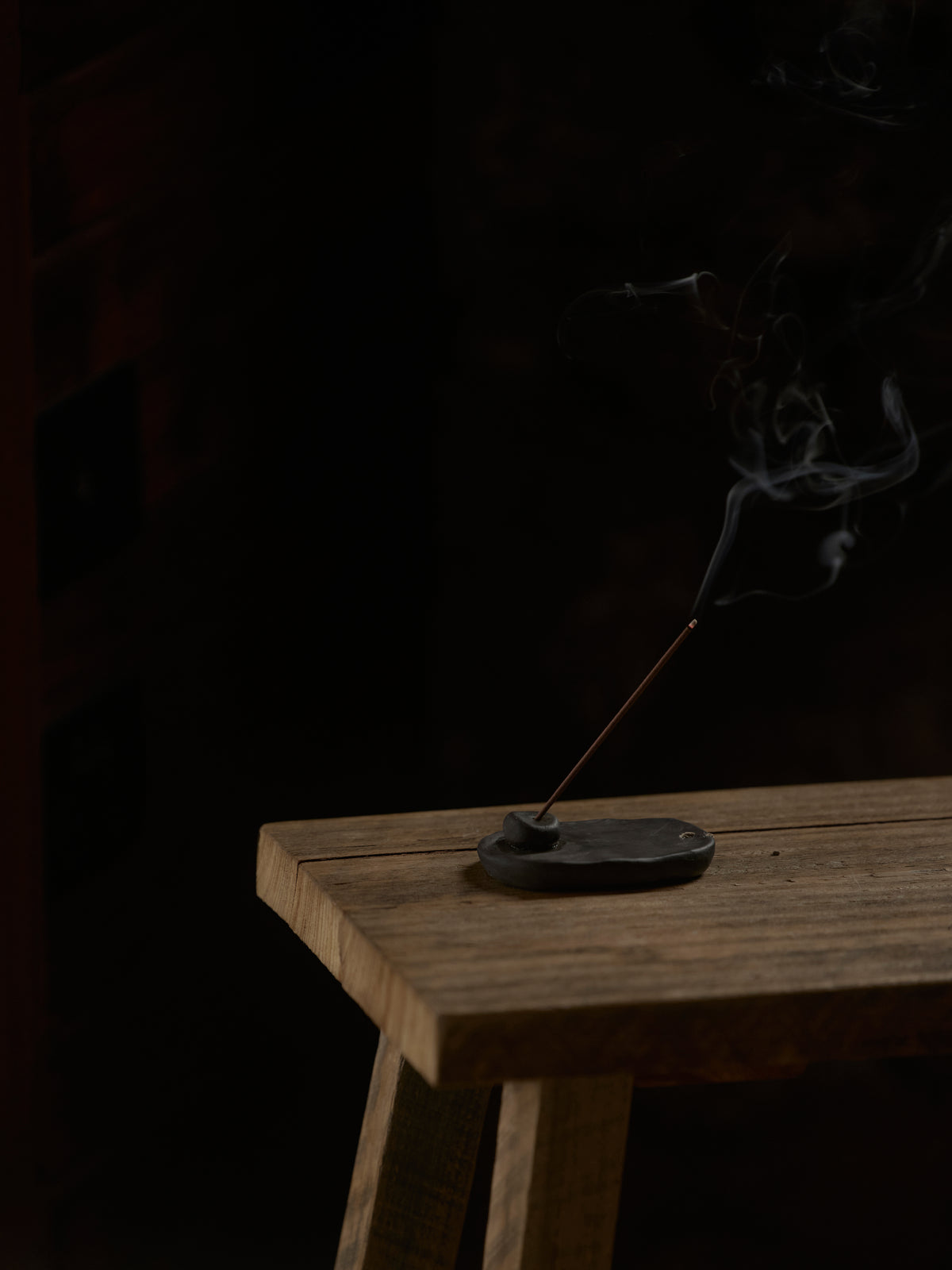 Incense stick burning on a wooden platform with a dark background
