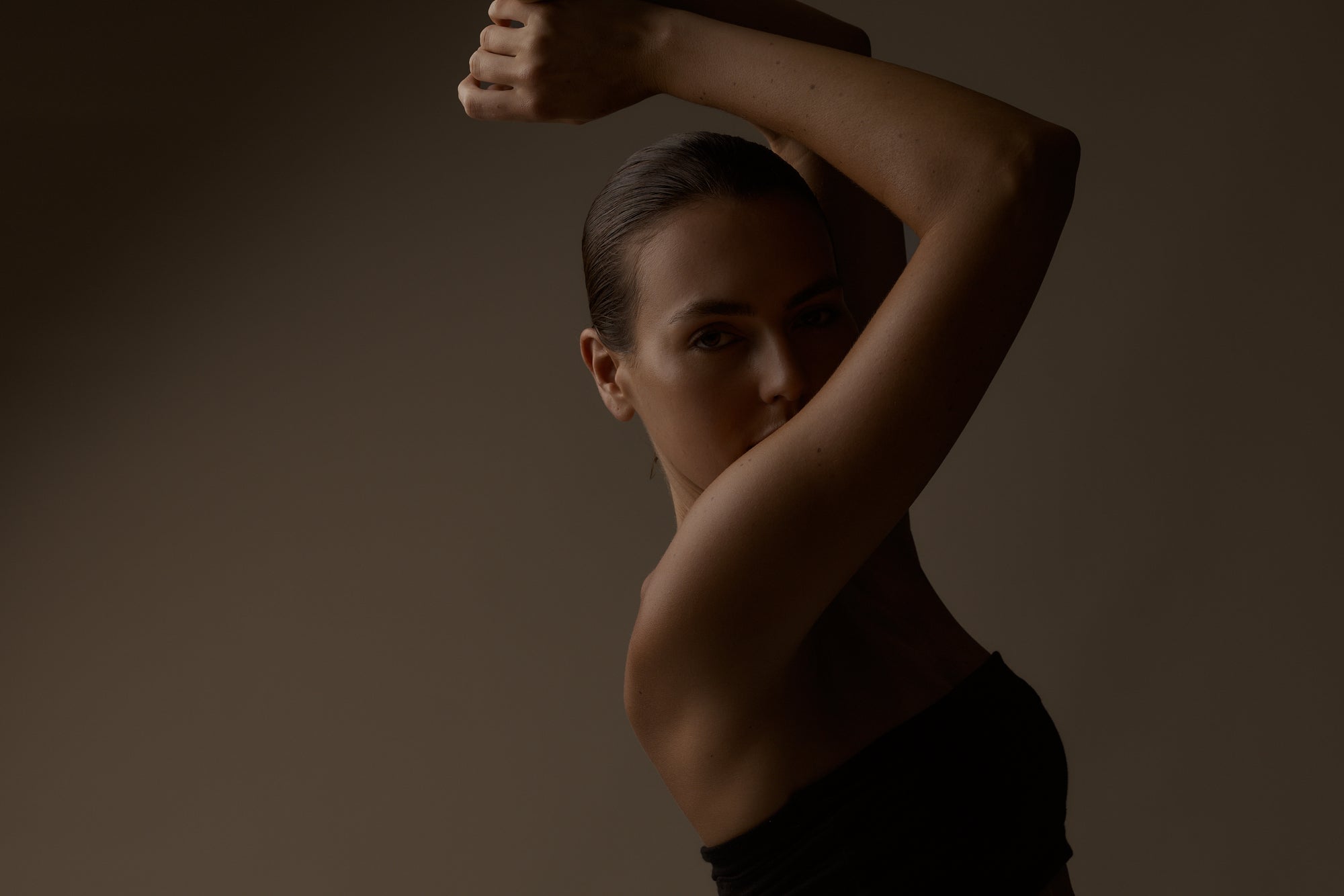 Woman posing with one arm raised against a dark background