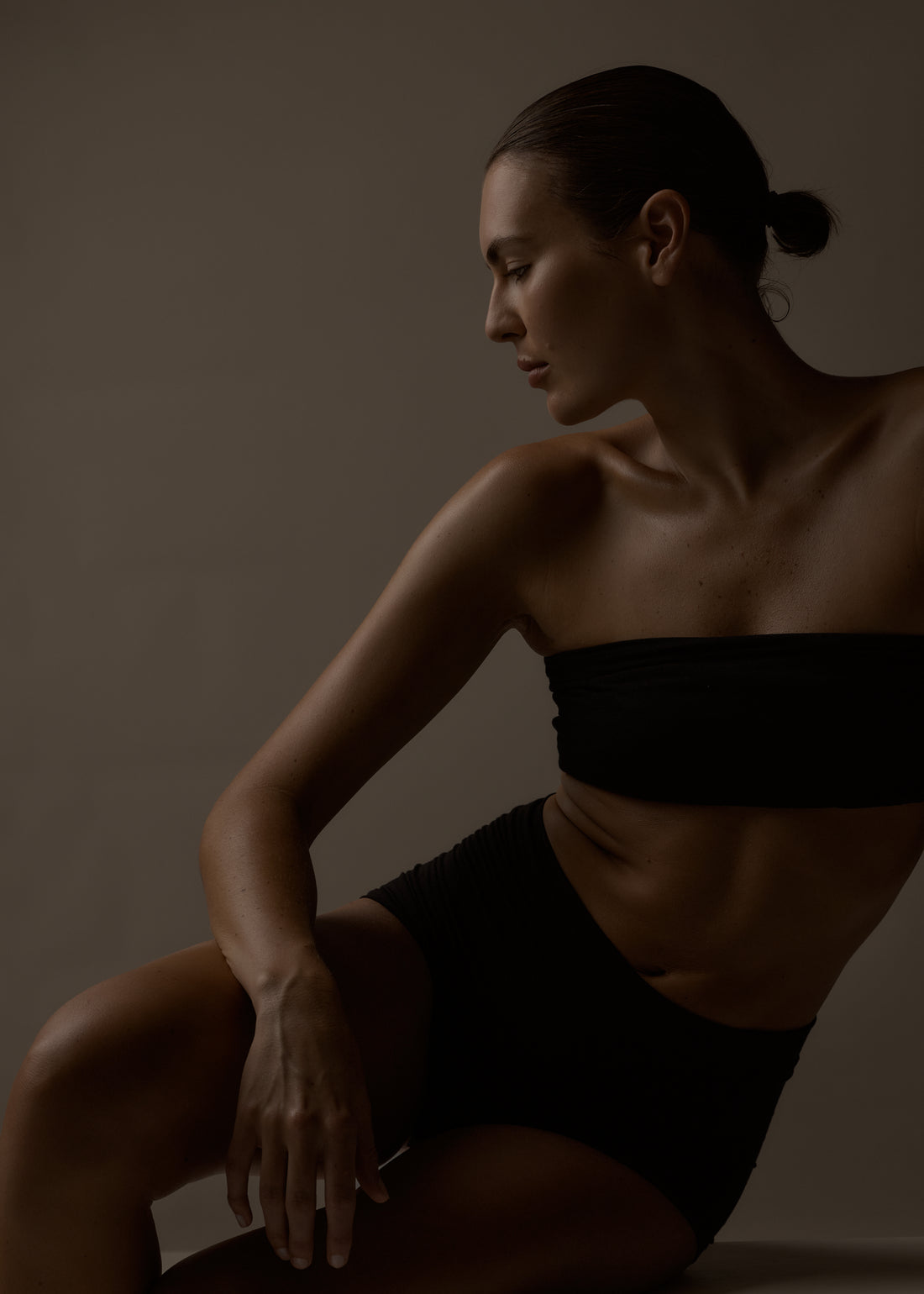 Woman in a black strapless top and black shorts sitting against a dark background
