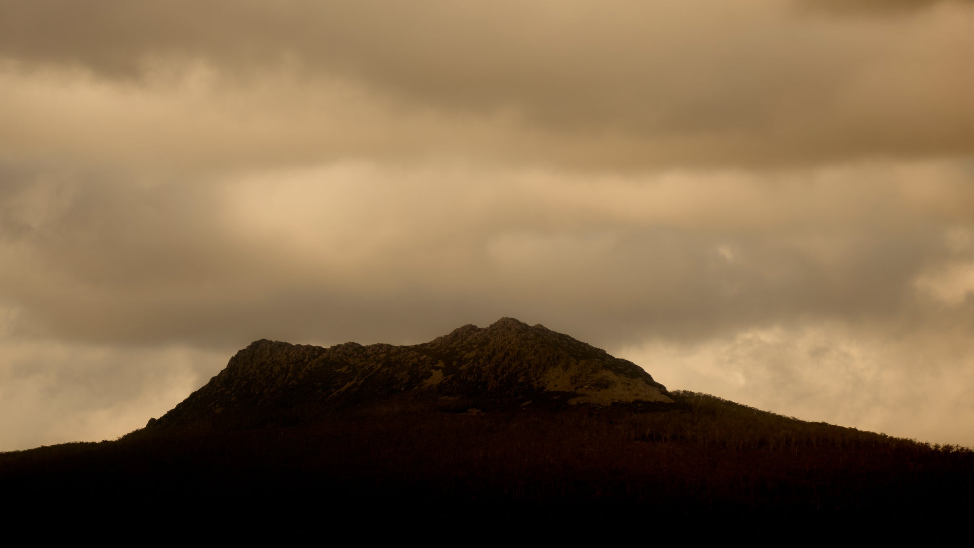 Silhouette of a mountain against a cloudy sky with a sepia tone